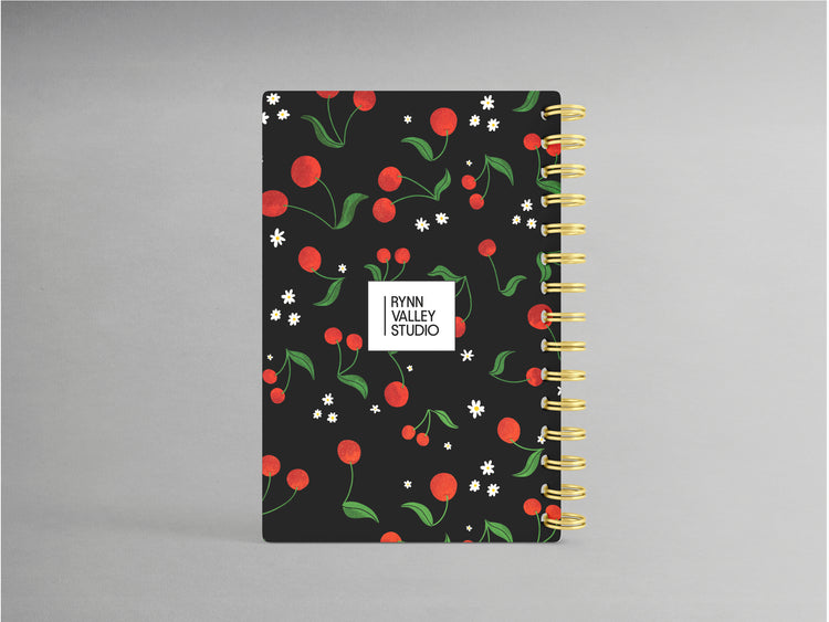 Embrace sophistication with this cherry-themed A5-sized hardcover spiral bound notebook, set against a sleek black background. Its design highlights a rich cherry motif, accented by a sturdy black spiral binding. Inside, enjoy the versatility of blank pages, ideal for jotting down notes, sketches, or creative inspirations with a touch of elegance.